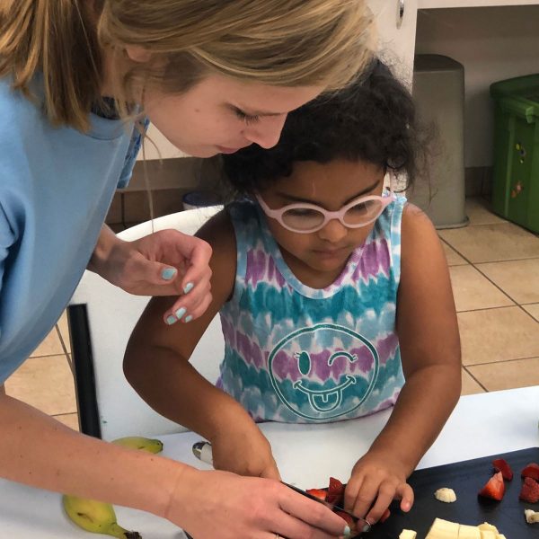 Volunteer helping young girl cut strawberries