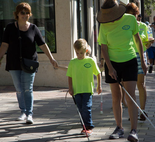 Volunteers helping kid walk with cane