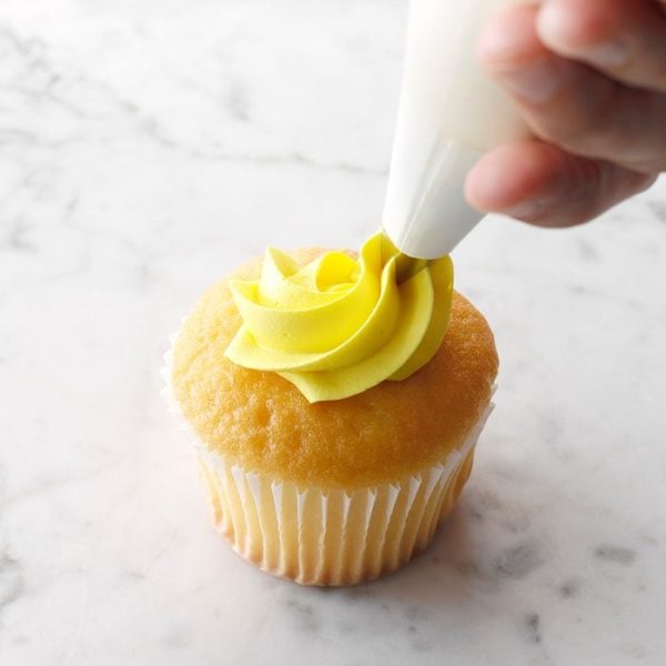 Piping yellow frosting onto vanilla cupcake